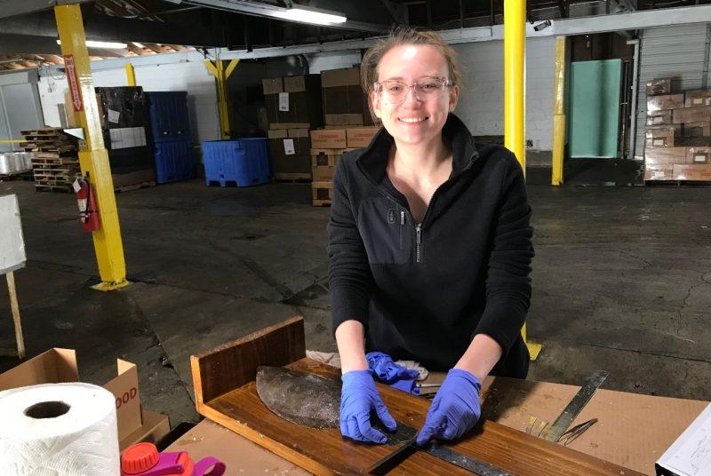 A person stands behind a table, holding a ruler to measure the size of a flounder.